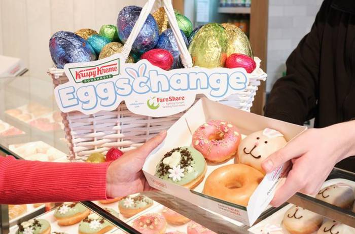 Krispy Kreme Eggschange basket of foil-wrapped chocolate eggs, with a hand holding a box of doughnuts: pink sprinkles, a bunny face, mint with daisies, and plain glazed.