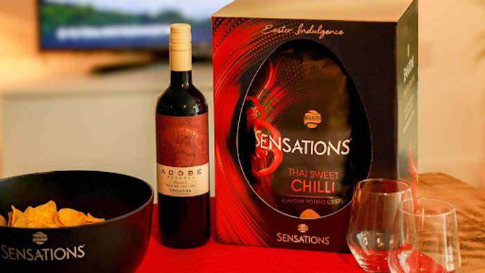 Sensations Thai Sweet Chilli Easter box beside a bowl of crisps, a bottle of Adobe red wine and two glasses on a red table