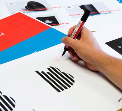 A person holding a red marker, circling a number on a printed sheet with charts, graphs, and colourful sections, on a wooden table.
