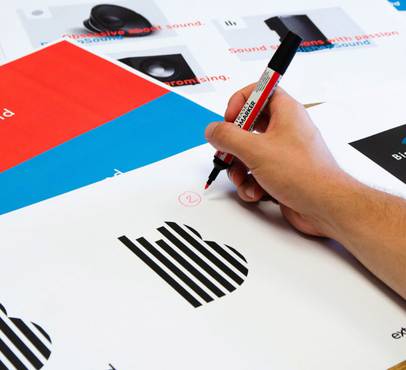 A person holding a red marker, circling a number on a printed sheet with charts, graphs, and colourful sections, on a wooden table.
