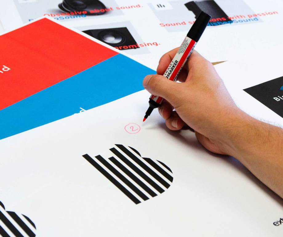 A person holding a red marker, circling a number on a printed sheet with charts, graphs, and colourful sections, on a wooden table.