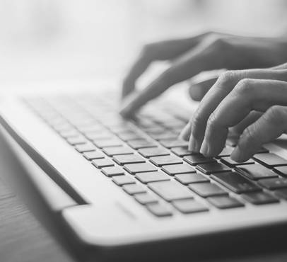 Hands typing on a laptop keyboard in black and white.
