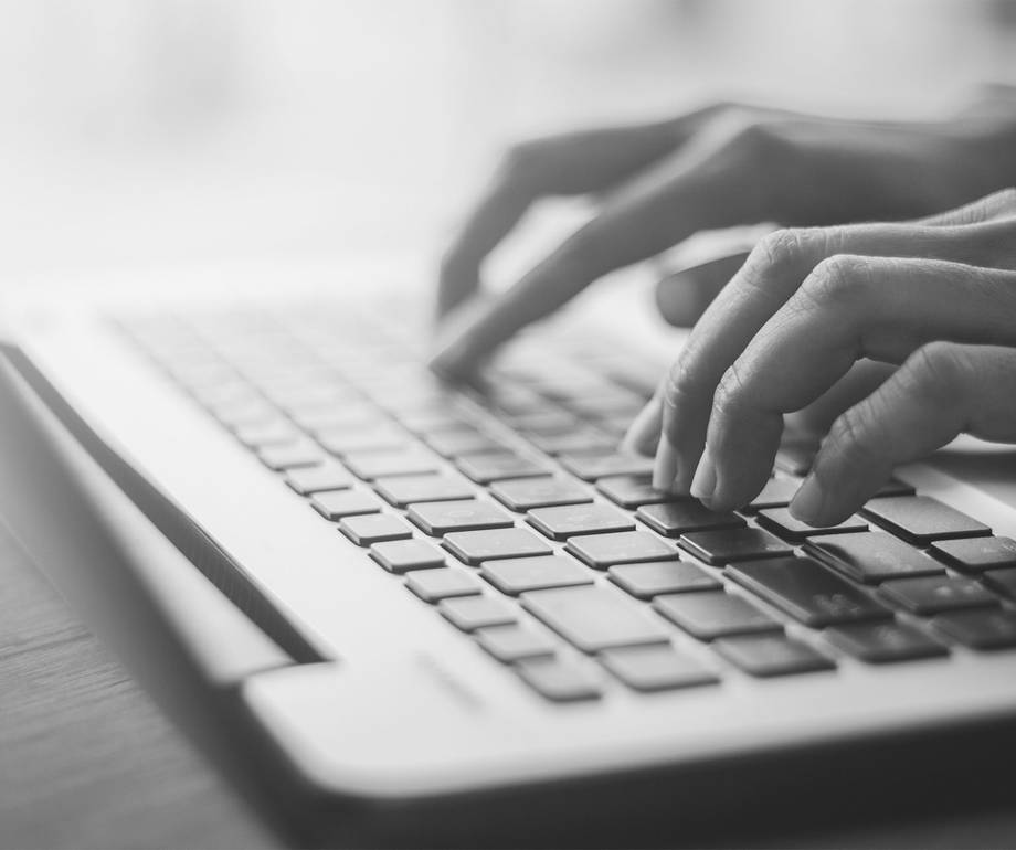 Hands typing on a laptop keyboard in black and white.