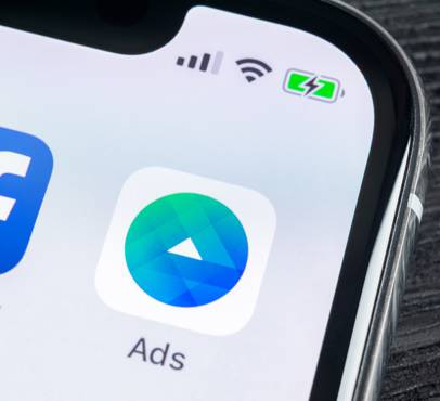 Close-up of a phone screen showing a partly cropped Facebook icon beside an Ads app icon with a green-blue gradient and white arrow, on a dark surface.