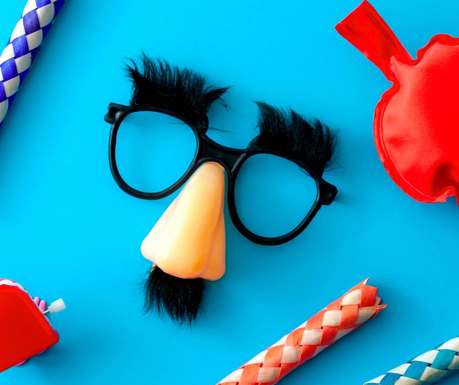 A novelty mask resembling a person's face, with glasses, a large orange nose, black bushy eyebrows, and a small black beard, alongside party props on a blue background.