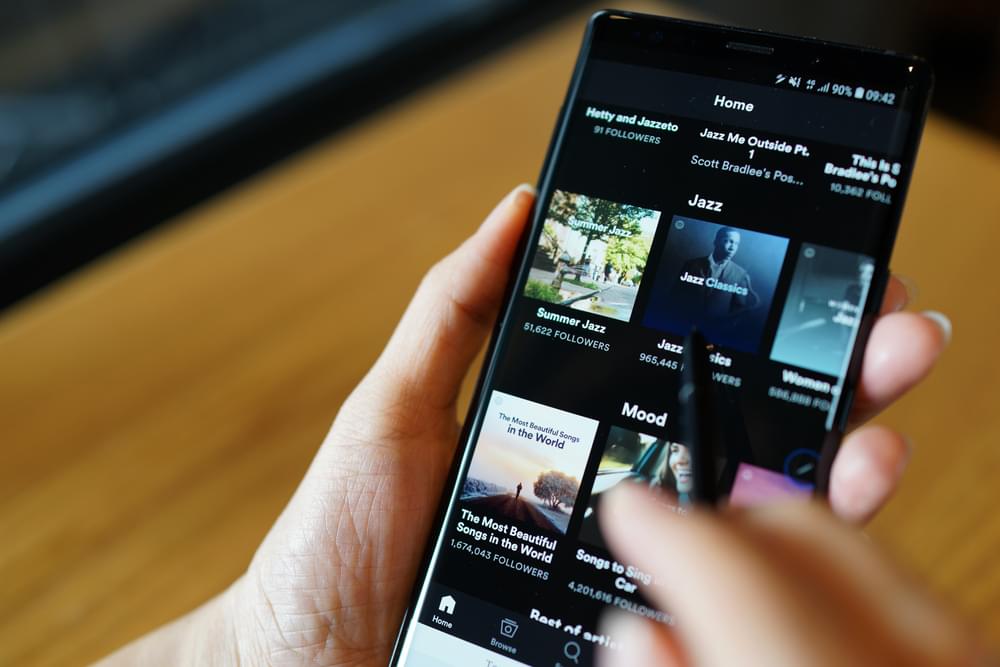 A close up shot of someone holding a mobile phone, with the screen showing the Spotify home page with a selection of music to choose from.