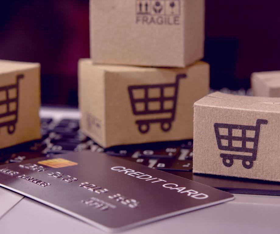 Small cardboard boxes with shopping cart symbols placed on a laptop keyboard along with a credit card.