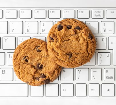 Two chocolate chip cookies resting on a white computer keyboard, filling most of the frame with the keys visible in the background.