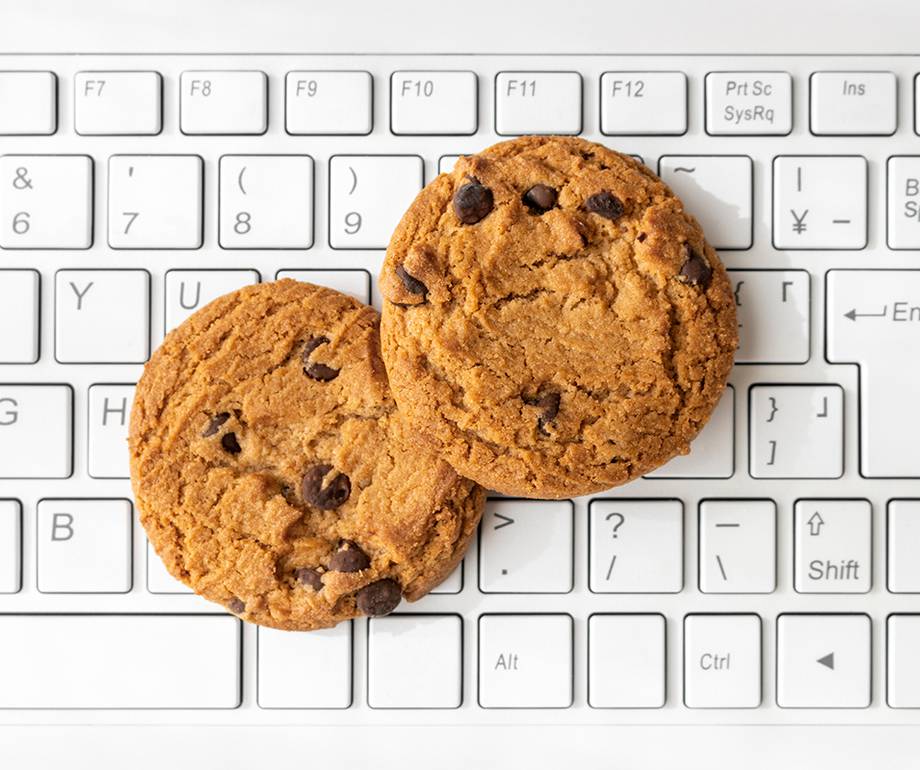 Two chocolate chip cookies resting on a white computer keyboard, filling most of the frame with the keys visible in the background.