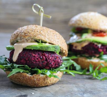 Vegetarian beetroot burger with arugula, cucumber, and creamy sauce on a wholemeal bun, placed on a rustic wooden surface.