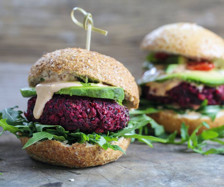 Vegetarian beetroot burger with arugula, cucumber, and creamy sauce on a wholemeal bun, placed on a rustic wooden surface.