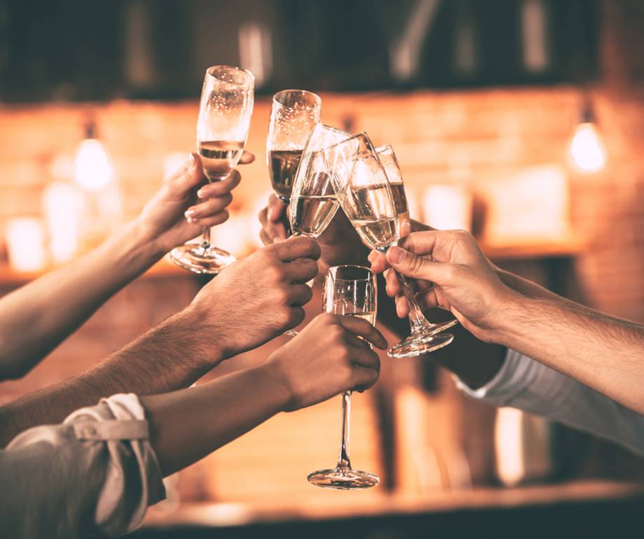 Hands raising glasses of champagne in a celebratory toast against a warm, softly blurred background.