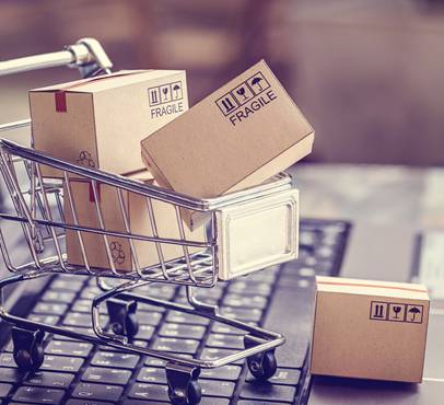 Miniature shopping cart with cardboard boxes labeled "fragile" on a keyboard background.