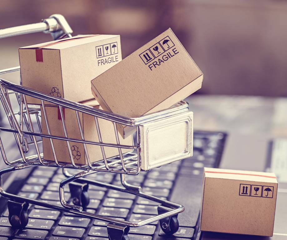 Miniature shopping cart with cardboard boxes labeled "fragile" on a keyboard background.