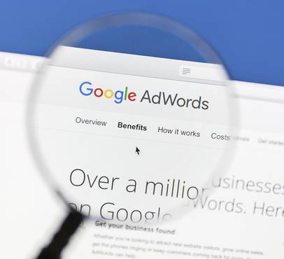 Close-up of a computer screen displaying the Google AdWords website through a magnifying glass.