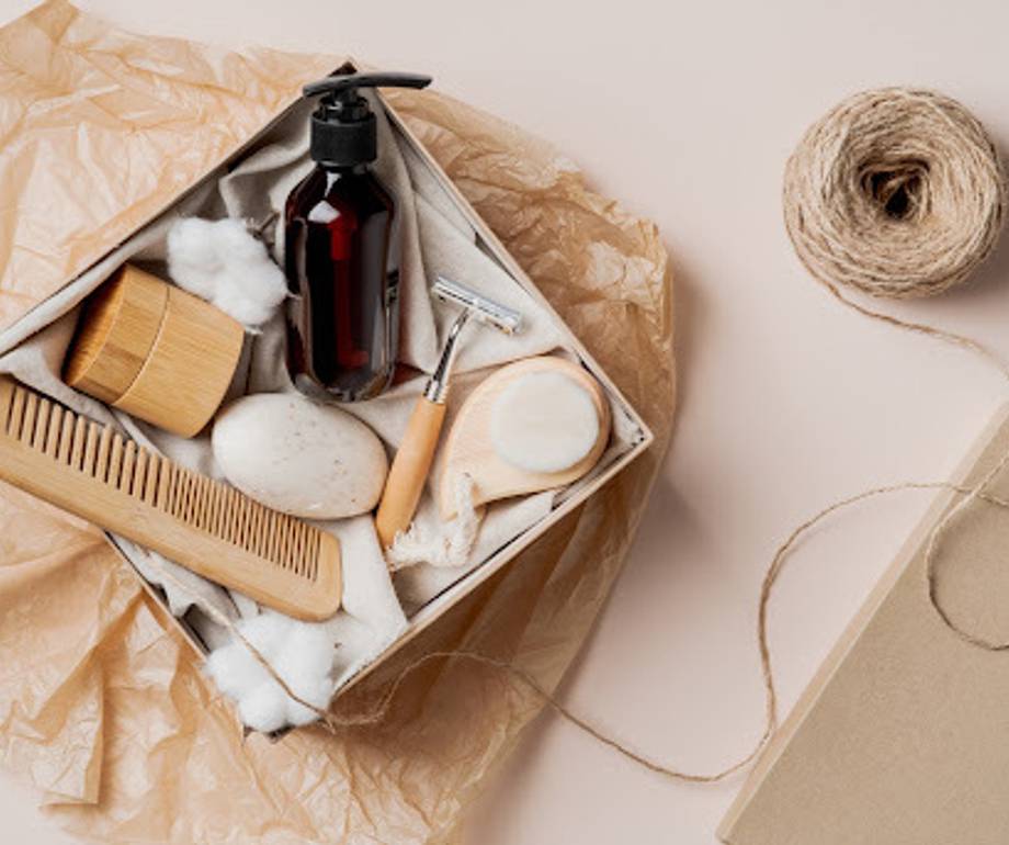 A collection of toiletries and grooming items, including a pump bottle, comb, natural sponges, and a roll of twine, arranged in a box with tissue paper.