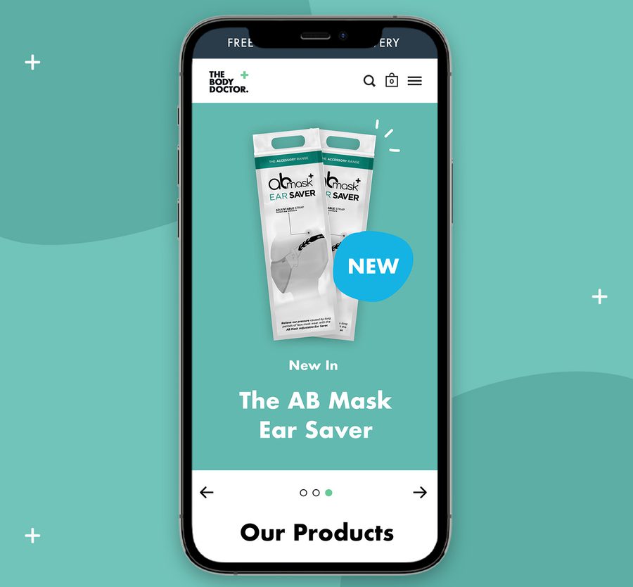 Smartphone displaying a website for The Body Doctor, highlighting the new AB Mask Ear Saver product on a teal background.