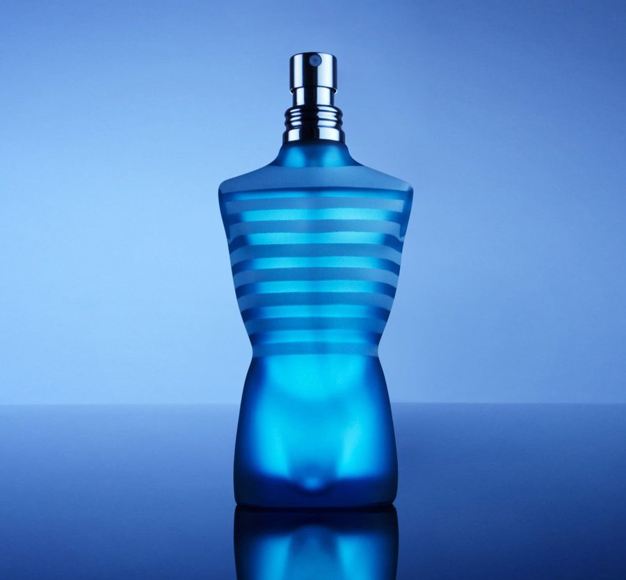 A blue perfume bottle with horizontal stripes, tapered shape, and silver spray nozzle, reflected on a glossy surface against a blue background.