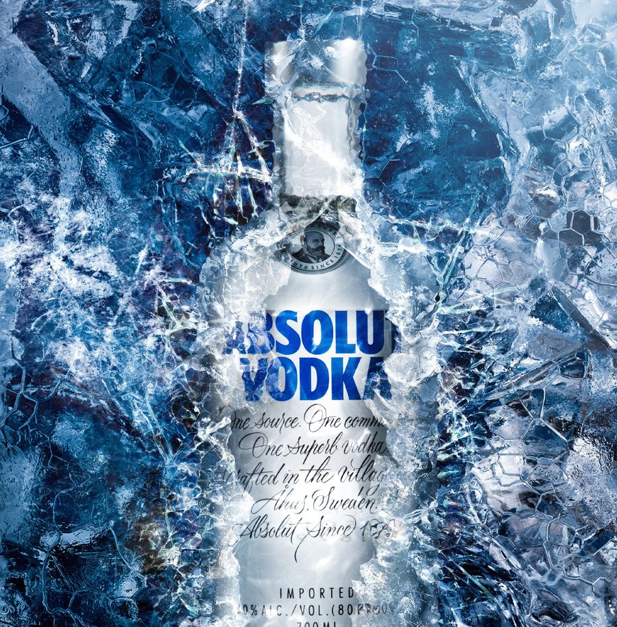 A vodka bottle is frozen behind shattered ice with an icy blue background, highlighting the label and brand name 'Absolut Vodka'.