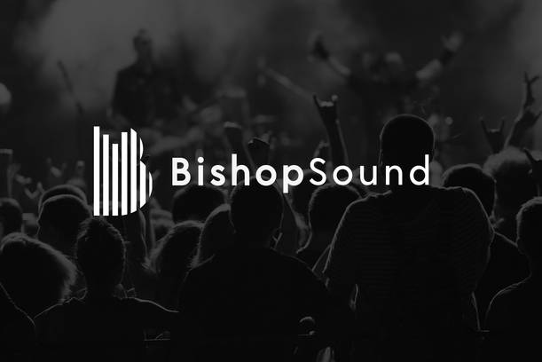 Crowd of people at a concert or event with musicians on stage performing, all in black and white, with the "BishopSound" logo overlayed in the centre.