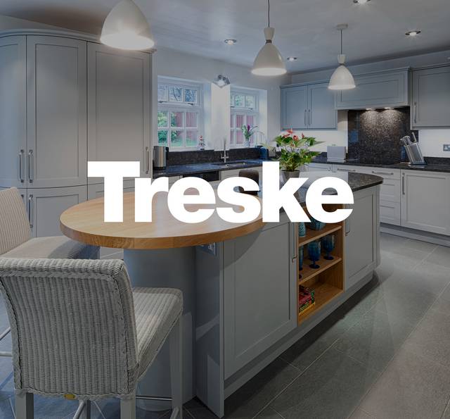 A modern kitchen with grey cabinets, black countertops, a centre island with open shelving, and a window above the sink, decorated with plants.