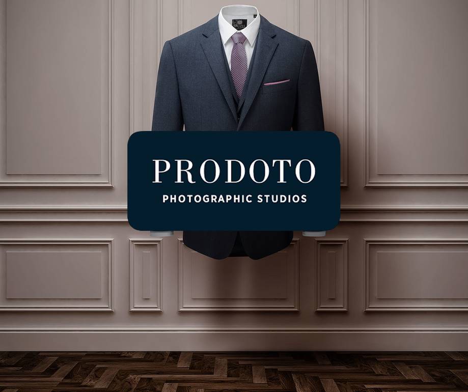 A suit jacket, shirt and tie hang on a wall with decorative paneling, with a "PRODOTO PHOTOGRAPHIC STUDIOS" sign in front.