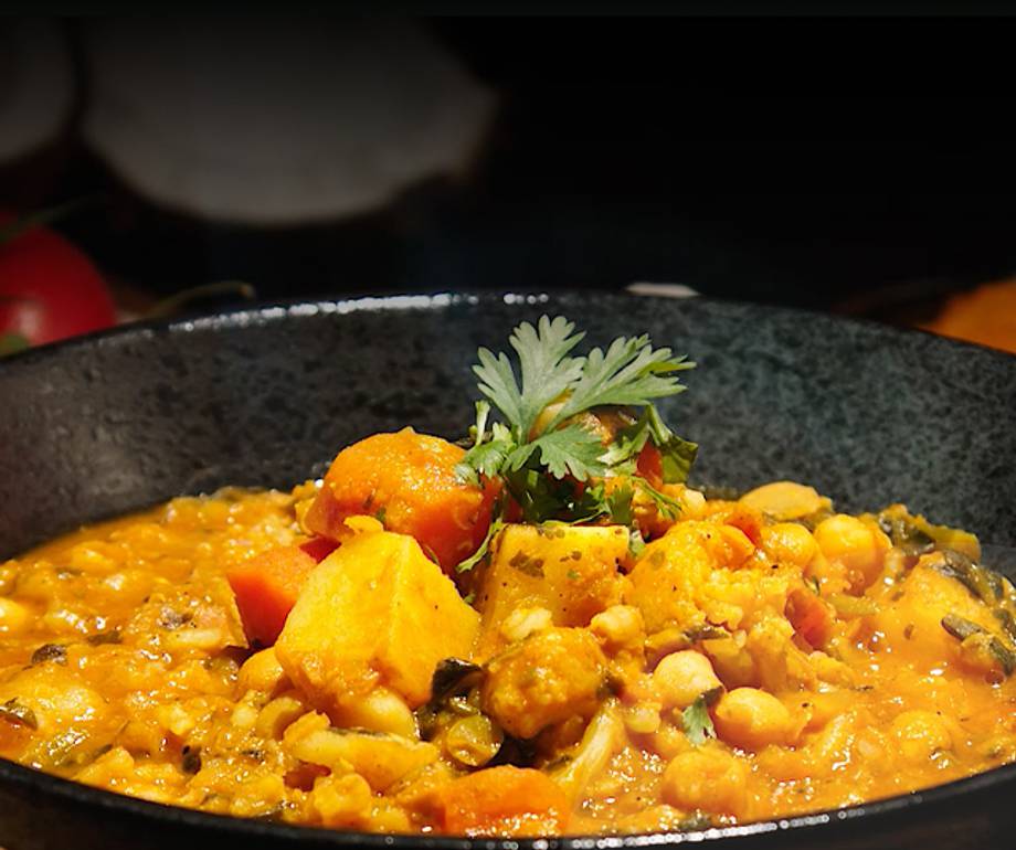 A bowl of vegetable and chickpea curry garnished with fresh coriander, with a dark background and steam rising from the dish.