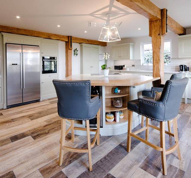 Modern kitchen with white cabinets, a central island with seating, stainless steel fridge, and wood accents on beams and flooring.