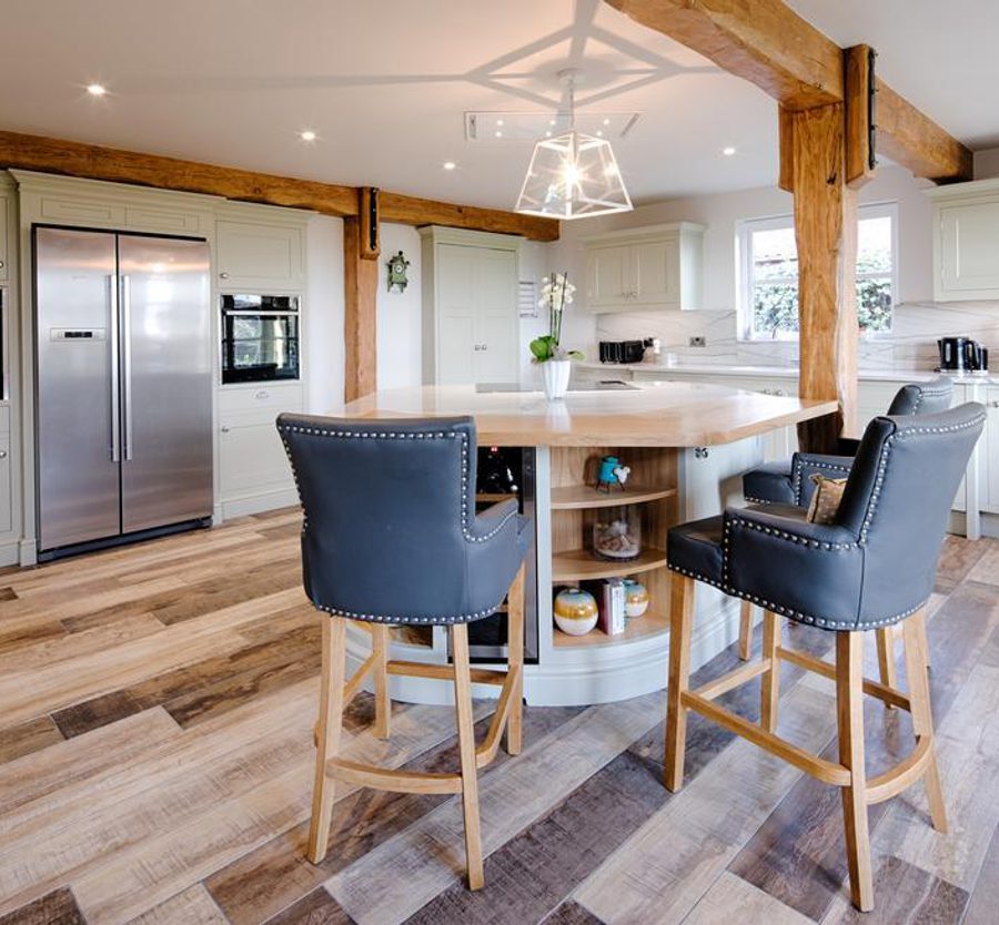 Modern kitchen with white cabinets, a central island with seating, stainless steel fridge, and wood accents on beams and flooring.