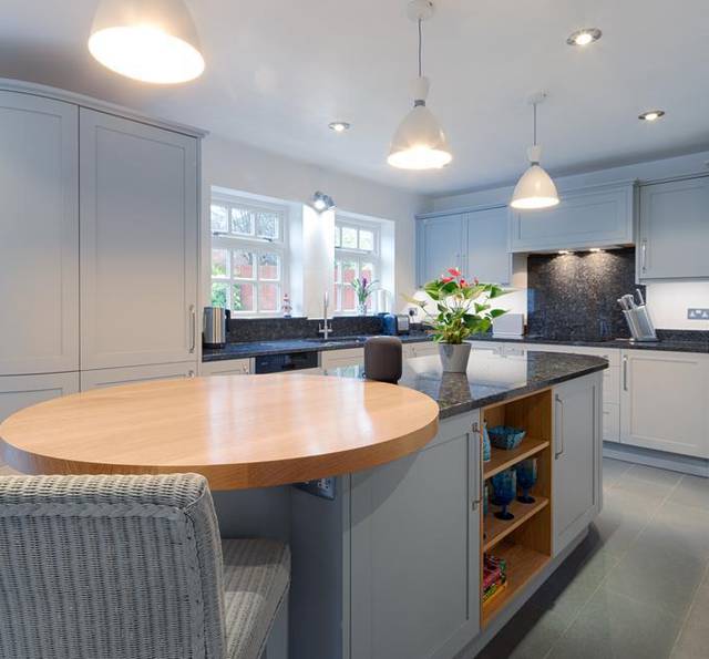 A modern kitchen with light blue cabinets, black countertops, pendant lighting, and a round wooden table with chairs.