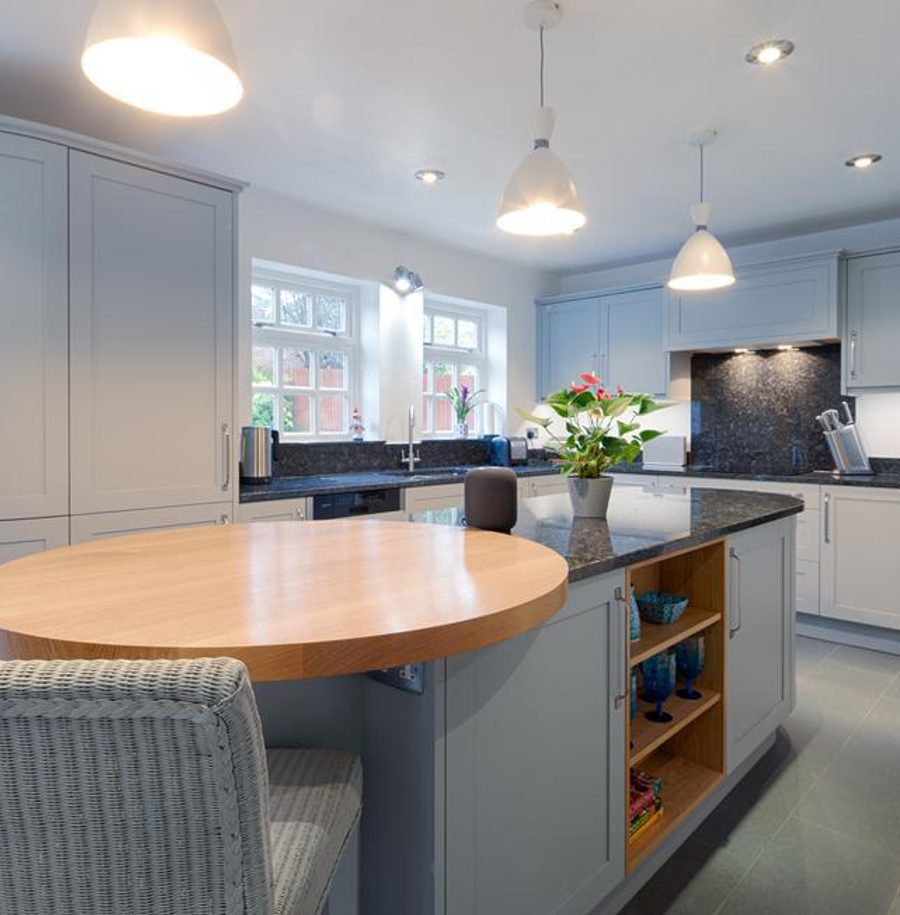 A modern kitchen with light blue cabinets, black countertops, pendant lighting, and a round wooden table with chairs.