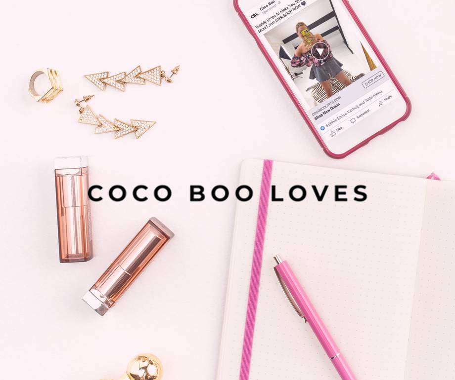 Pink phone displaying a woman taking a mirror selfie, some gold and rhinestone jewelry, a pink pen, and a dotted notebook on a white background.