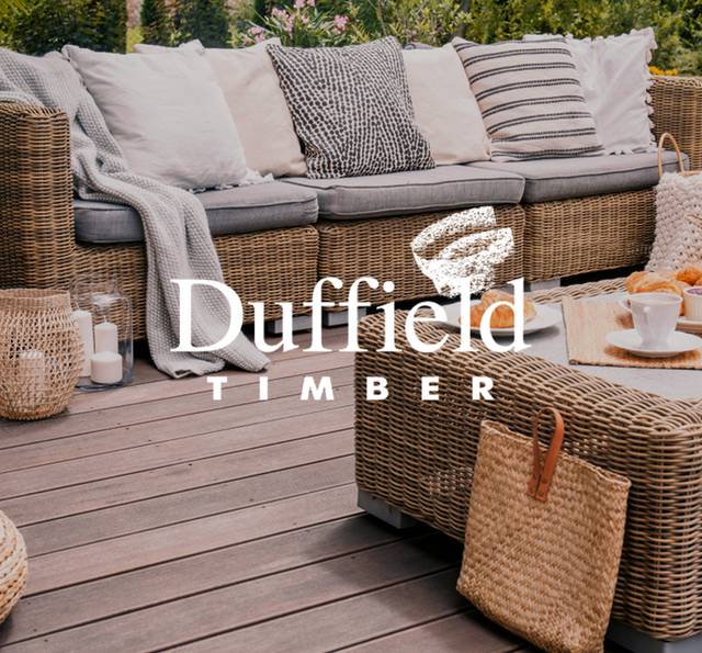 Outdoor patio with a wicker sofa, grey cushions and a striped throw, a wicker coffee table with croissants and tea, on timber decking. White "Duffield Timber" logo overlaid.