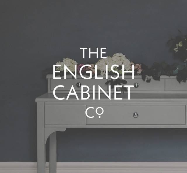 A grey sideboard with flowers on top against a dark wall, overlaid with text reading 'The English Cabinet Co.' in white.