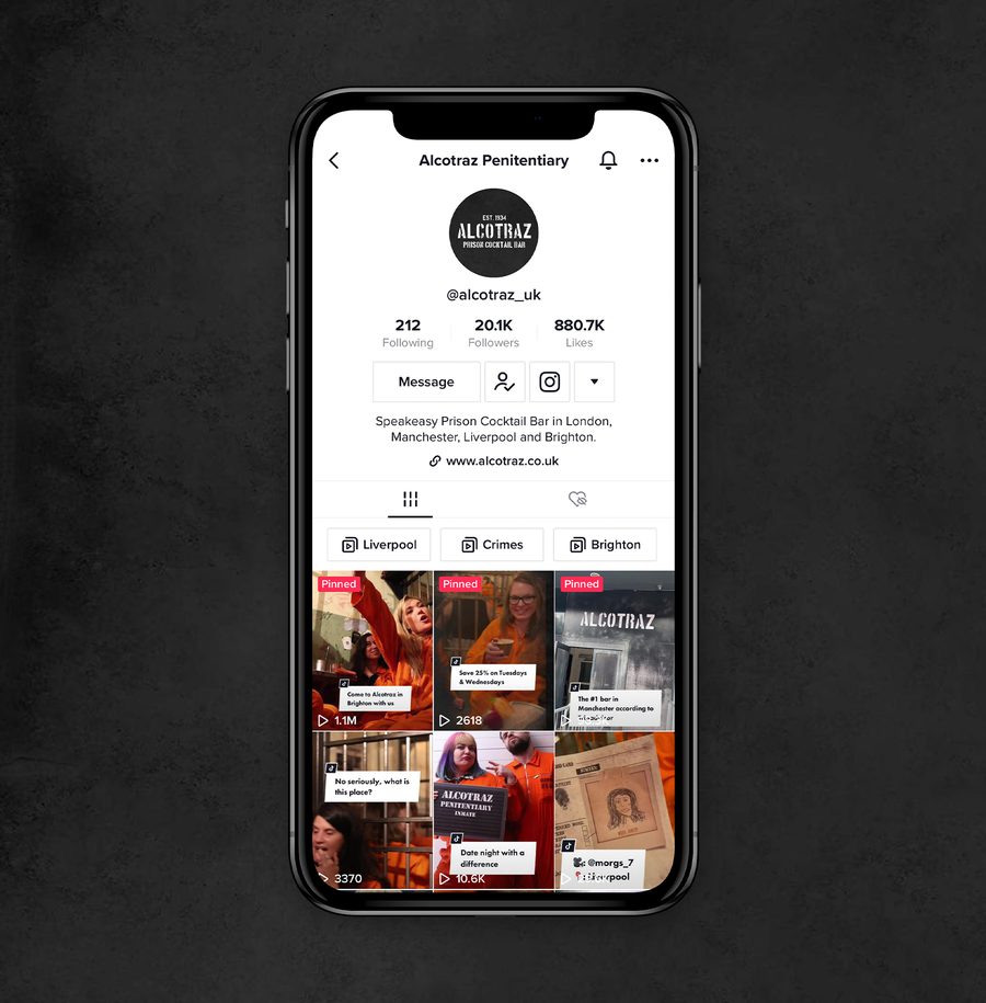 A smartphone displaying a TikTok profile for Alcotraz Penitentiary with videos featuring people at a prison-themed bar, against a dark textured background.