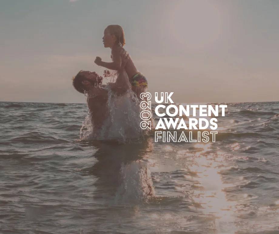A person lifting a child in the sea during sunset, with "2023 UK Content Awards Finalist" text overlayed on the right side.