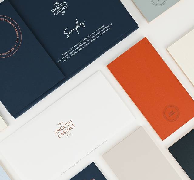 Flat lay of various colour swatches and booklets from The English Cabinet Co, featuring navy, white, orange, and light grey colours on a white background.