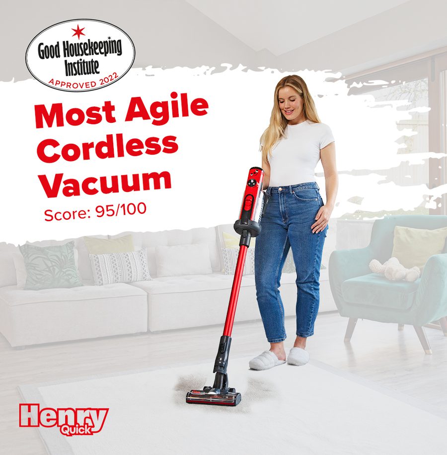 Young woman standing with a cordless vacuum cleaner in a bright living room, smiling, wearing casual white top and jeans.