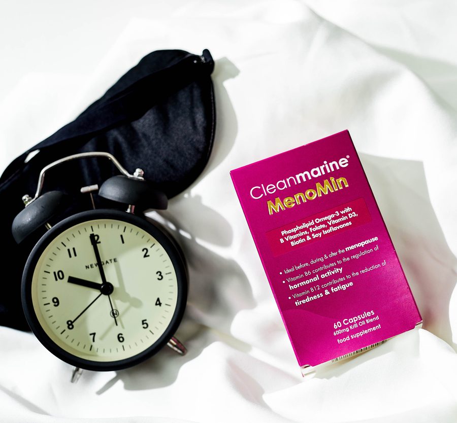 A black alarm clock showing 11:59, a pink box of Clearmarine Menomin supplements, and a black pouch on a white surface.