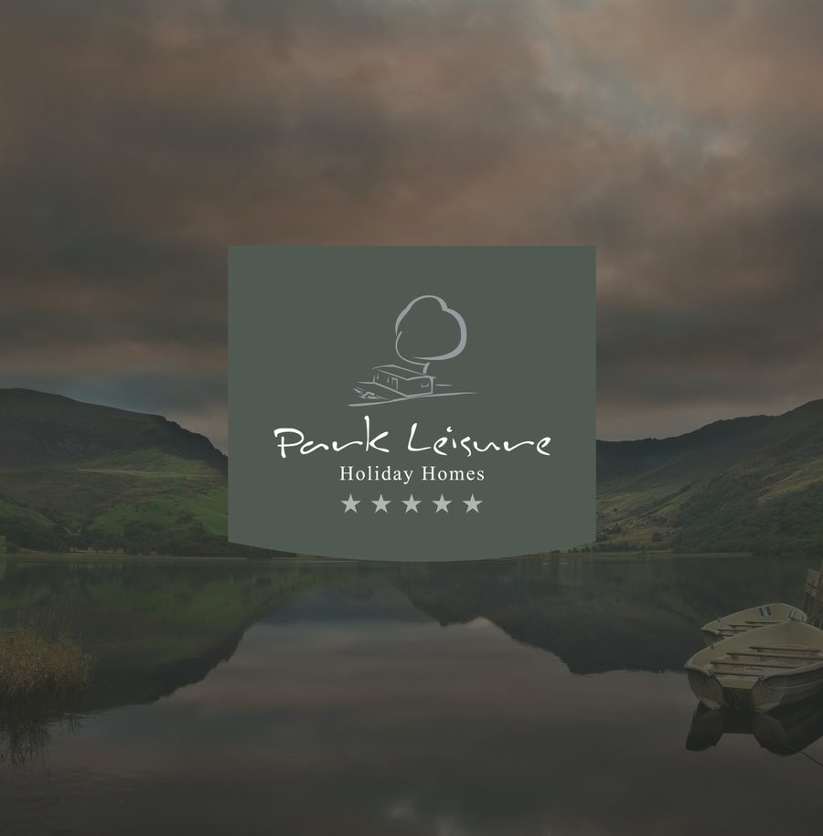 Scenic lake with boat and hills, cloudy sky, and a central overlay featuring 'Park Leisure Holiday Homes' logo with stars.