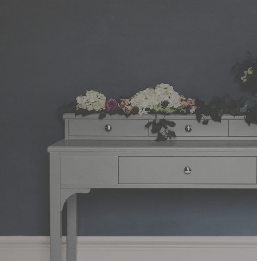White dresser with a bouquet of white, pink, and purple flowers on top against a dark teal wall.