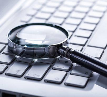 A magnifying glass resting on a computer keyboard, with a focus on the keys and a slightly reflective surface.