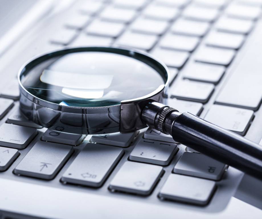 A magnifying glass resting on a computer keyboard, with a focus on the keys and a slightly reflective surface.