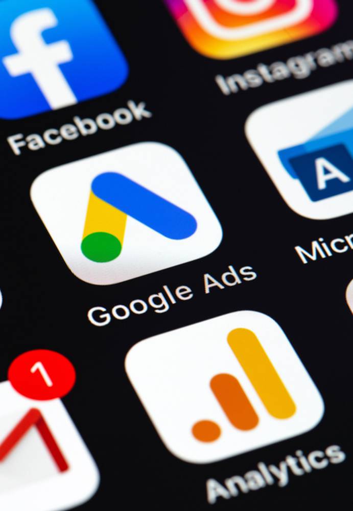 Smartphone screen displaying various social media, advertising, and analytics app icons including Facebook, Instagram, Google Ads, Microsoft Ads, and Gmail.