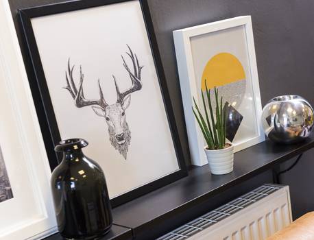 Decorative wall shelf with framed artwork, a black vase, a white pot with a green plant, and a reflective silver vase.