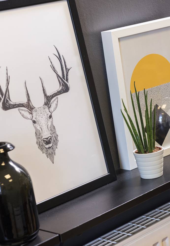 Decorative wall shelf with framed artwork, a black vase, a white pot with a green plant, and a reflective silver vase.
