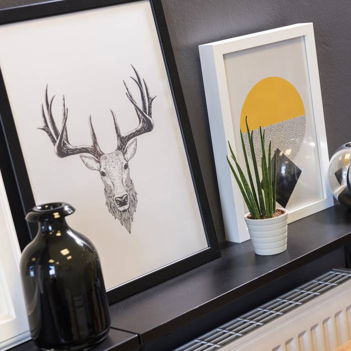 Decorative wall shelf with framed artwork, a black vase, a white pot with a green plant, and a reflective silver vase.
