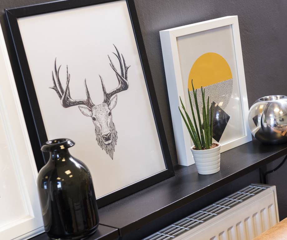 Decorative wall shelf with framed artwork, a black vase, a white pot with a green plant, and a reflective silver vase.