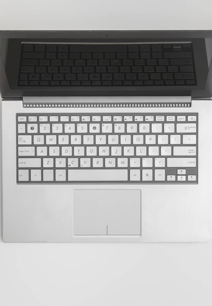 Open laptop, smartphone, cup of coffee, notebook with pen, and a plant arranged on a white desk.