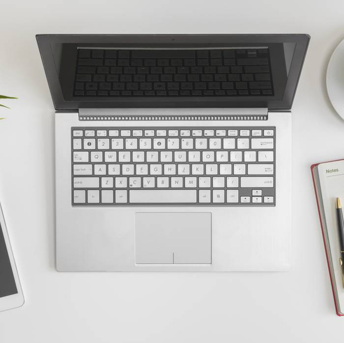 Open laptop, smartphone, cup of coffee, notebook with pen, and a plant arranged on a white desk.